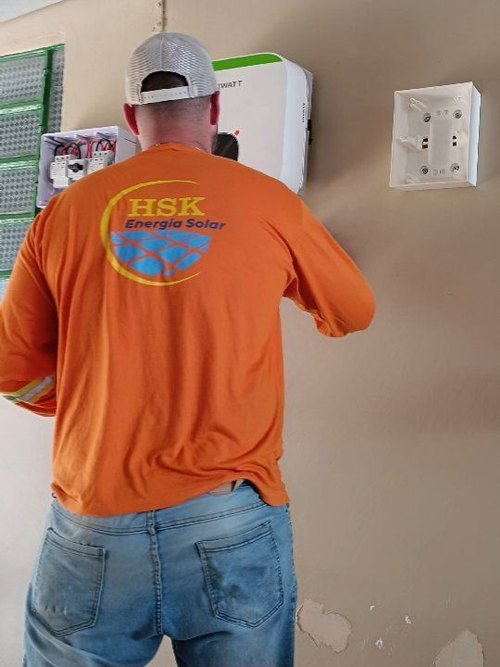 Técnico da HSK, de camiseta laranja, trabalhando em um quadro de distribuição.