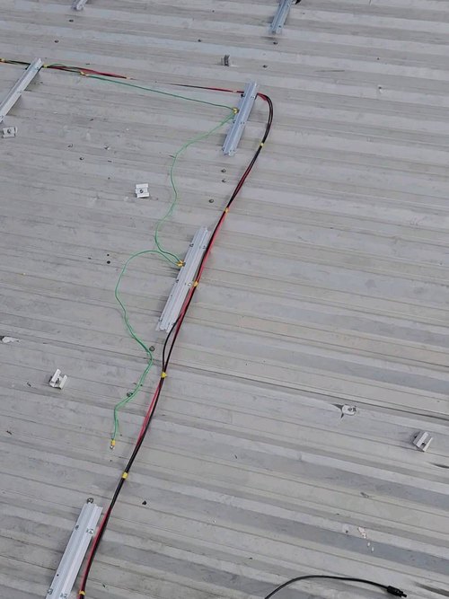 Cabeamento e trilhos de fixação em telhado metálico, obra em andamento.