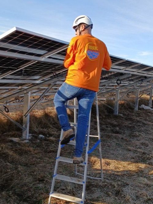 Técnico de capacete em escada, junto a uma usina solar de solo em campo aberto.